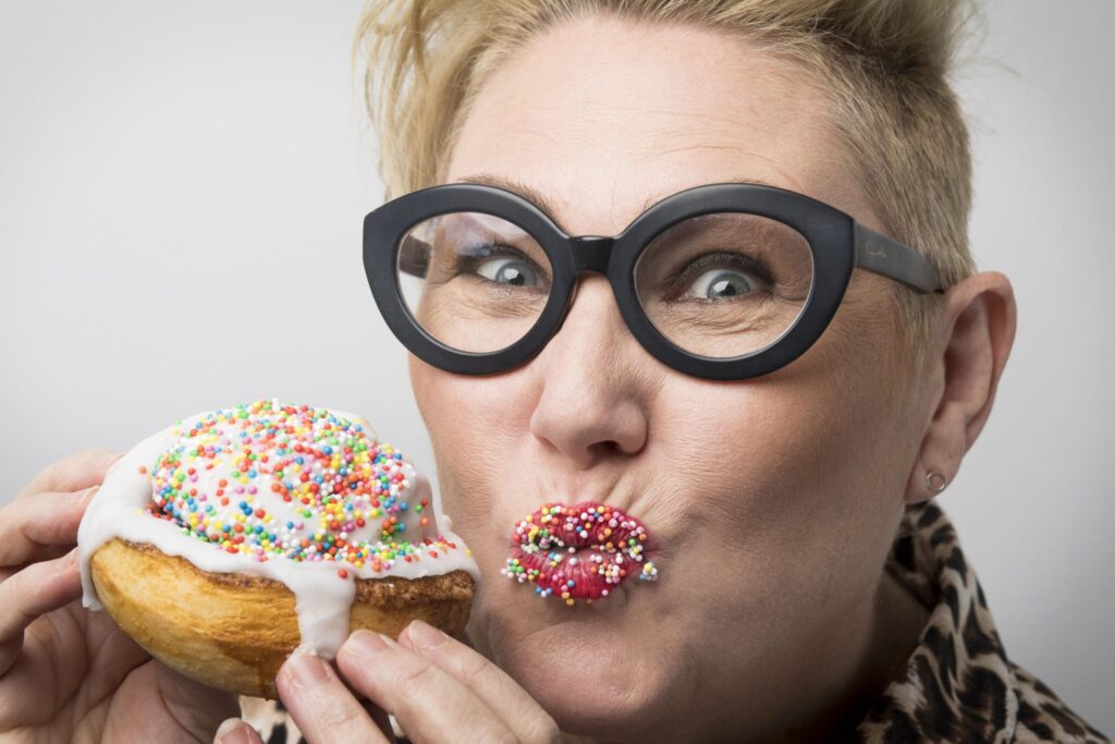 Woman with glasses eating colorful sprinkled donut.